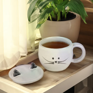 cute cat mug with lid, filled with tea on a side table.