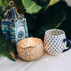 Side table arrangement with ceramic mug in raindrop pattern, candle, and plants.