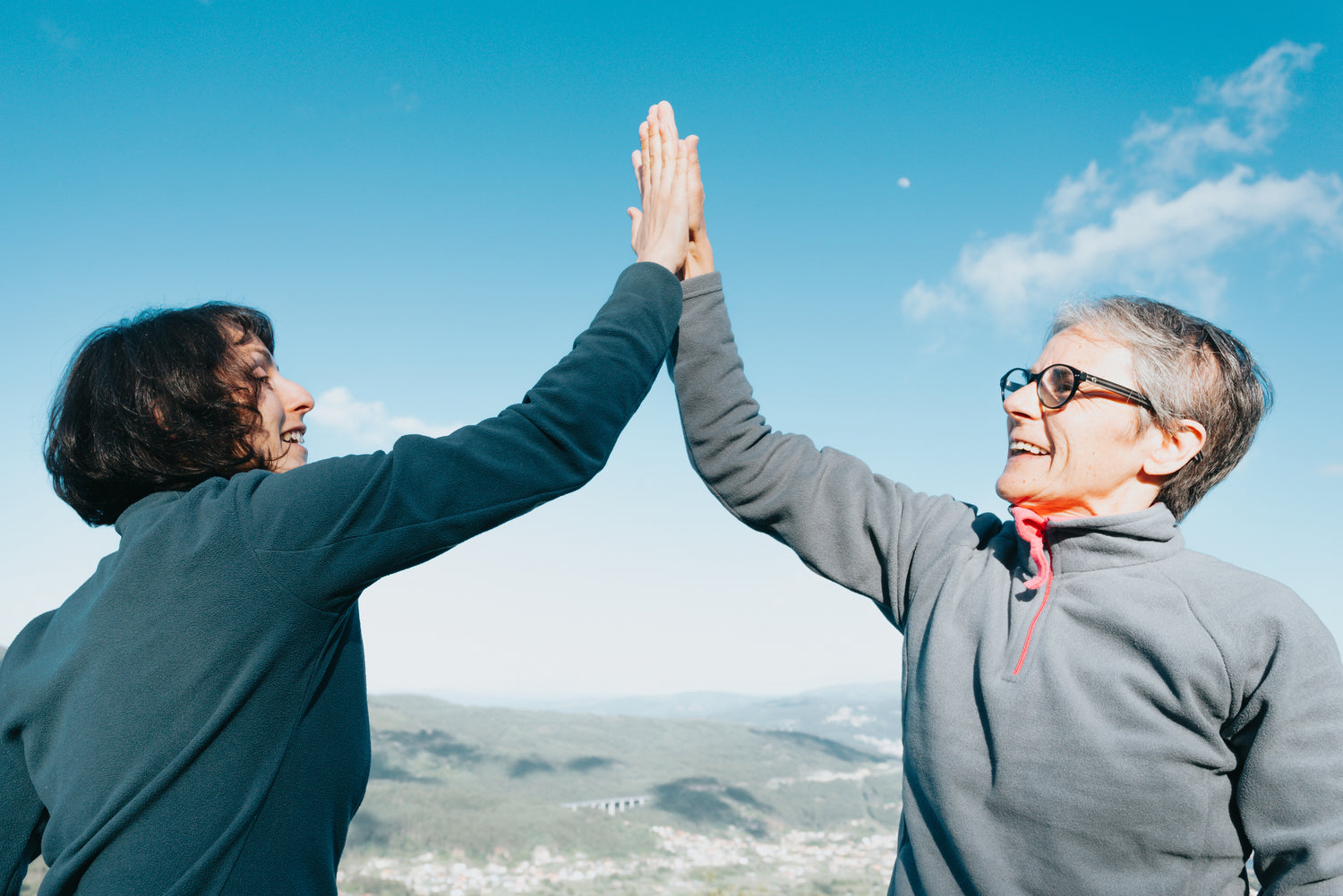 Two women giving a high five, with an open sky behind them.