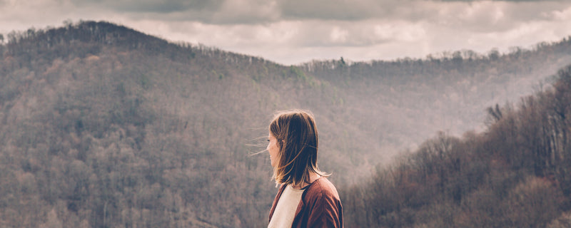 Woman looks out over mountain view, misty forest.
