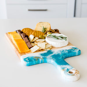Acacia Resin Cheeseboard in teal, white, and gold, with fruits and cheese on it.