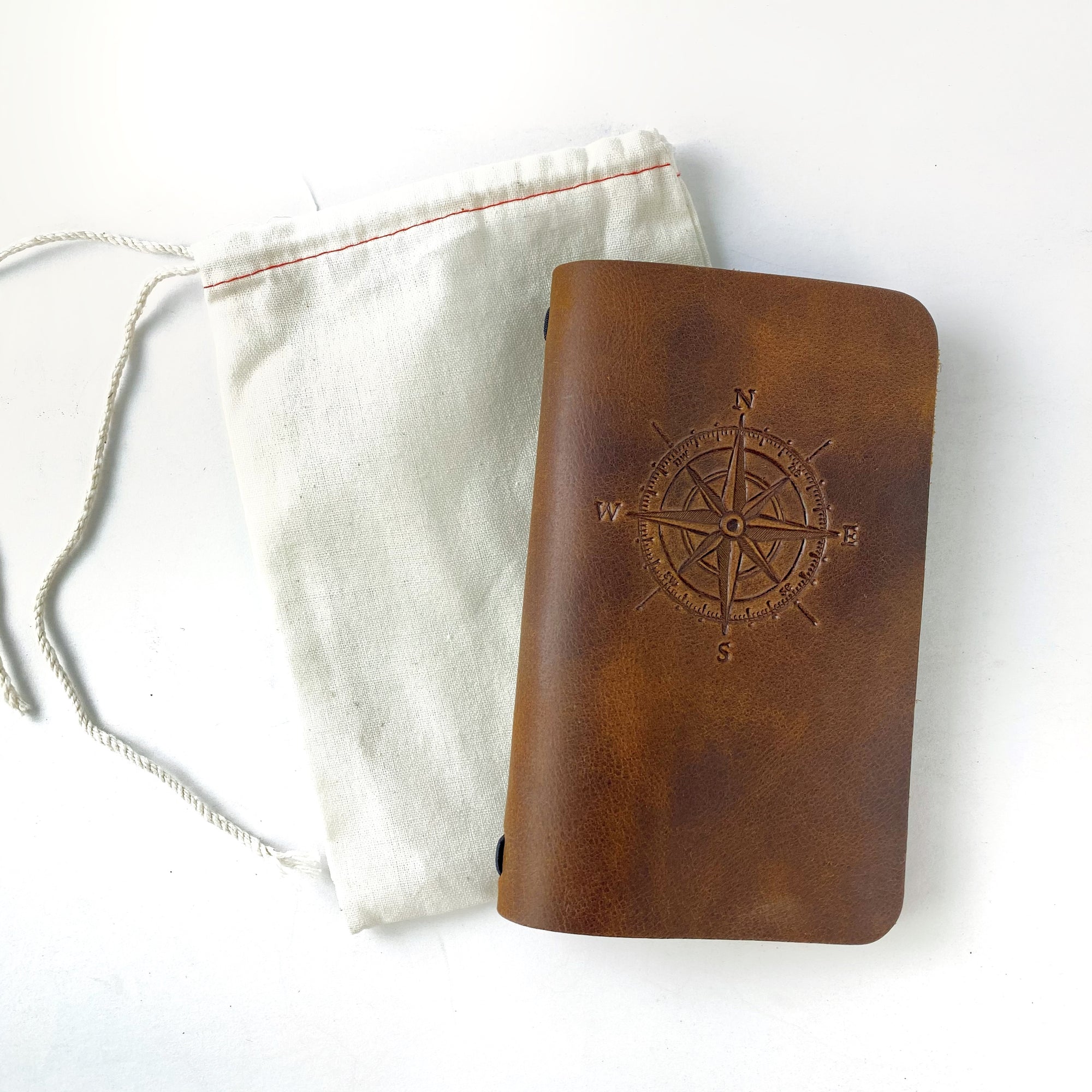Leather journal with compass engraving alongside canvas pouch.